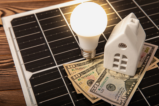 Flat lay composition with solar panel, LED lamp, piggy bank, house model and money on  texture background. Save money and clean energy concept. Ecology and sustainable development concept.