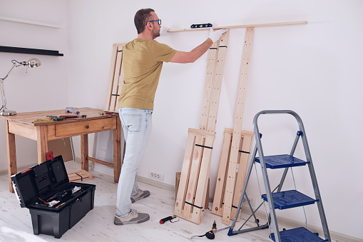 Man assembling new wooden shelf and furniture in the apartment.