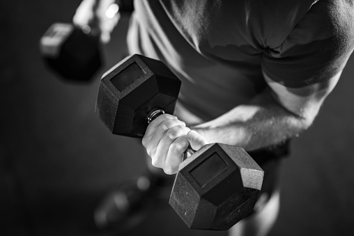 Black and white photo showcasing a handsome young man passionately engaged in a rigorous dumbbell workout, sculpting his physique