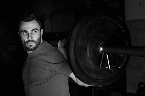 Dedicated male athlete excelling in cross training by lifting heavy barbells, symbolizing strength and determination, black and white photo