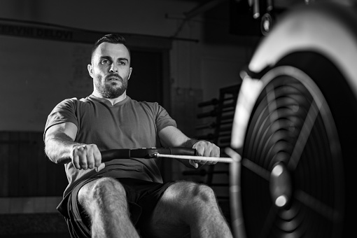 Young man excelling in a rowing machine exercise during cross training, dynamic black and white photo