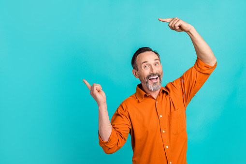 Photo of impressed funky guy wear orange shirt showing two fingers empty space isolated teal color background.