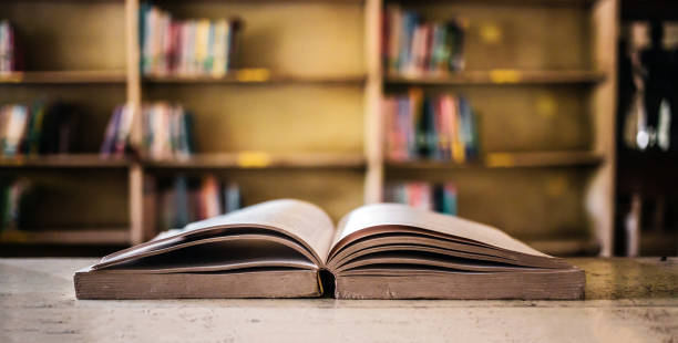 istock On a wooden table, there's an open book with a library visible in the background. A stack of books nearby adds to the theme of educational learning. 1638107082