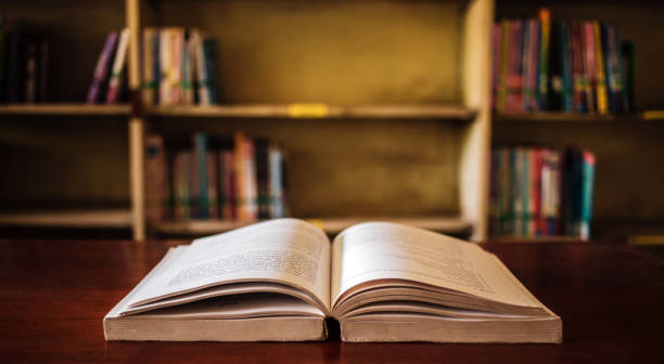 istock On a wooden table, there's an open book with a library visible in the background. A stack of books nearby adds to the theme of educational learning. 1638107601