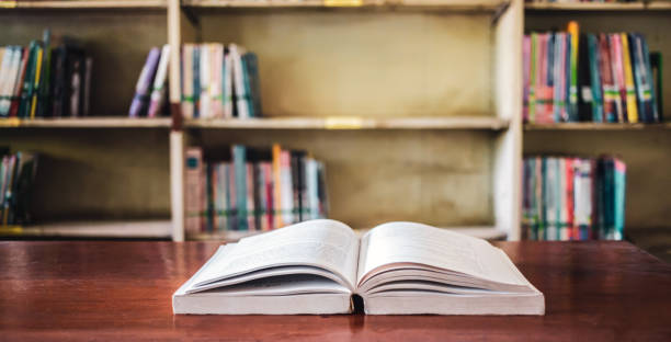 istock On a wooden table, there's an open book with a library visible in the background. A stack of books nearby adds to the theme of educational learning. 1638107603