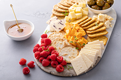 Cheese board or snack board with crackers, cheese, olives and raspberries