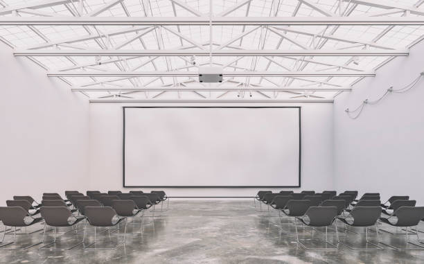 istock Front view (a closer look) of an empty white large gallery/showroom interior with seats, and a wide projection screen in the middle for events under a ceiling industrial construction 1638145452