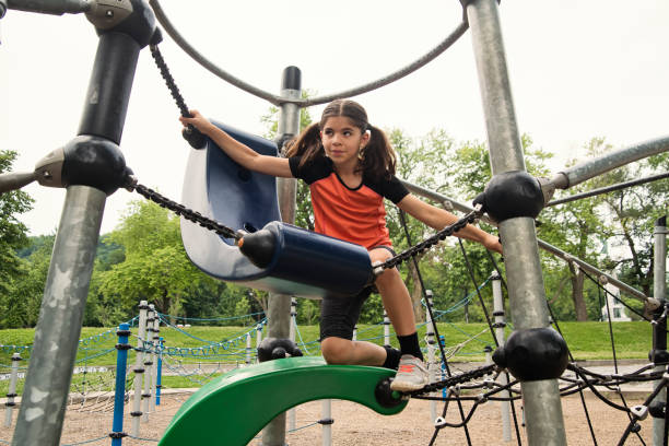 Young active girl of middle-eastern ethnicity in the playground in public park. She has long brown hair and is wearing active wear. Horizontal full length outdoors shot with copy space. This was taken in Montreal, Quebec, Canada.