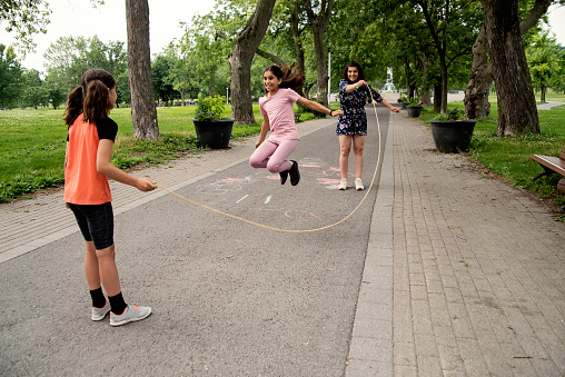 Mother of middle-eastern ethnicity playing with two active daughters in park. She is in her early forties, girls are 8 and 9 year’s old. They are playing with a jumping rope. Horizontal full length outdoors shot with copy space. This was taken in Montreal, Quebec, Canada.