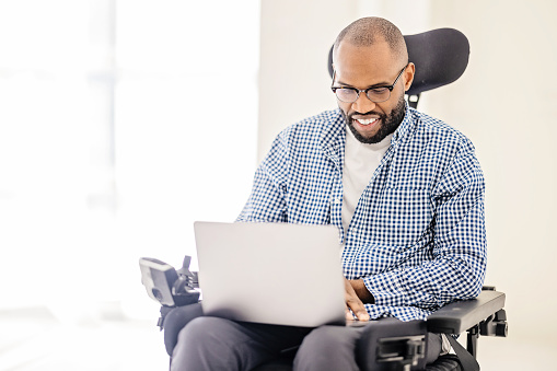 A wheelchair-bound black man is gazing at his laptop screen