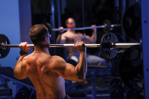 Back muscles of a man sitting in a fitness and lifting weights. Dumbbells or weightlifting training. Blue color fitness.