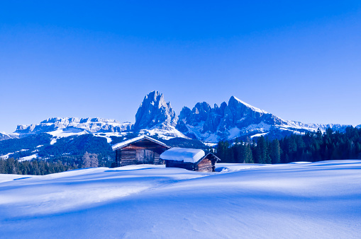 Snowy mountain huts on the Seiser Alm, Dolomites, South Tyrol, North Italy. In the backround the Sella Group, Langkofel and Plattkofel.