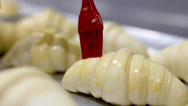 Close-up of an unrecognizable baker spreading egg yolks on croissants before baking them