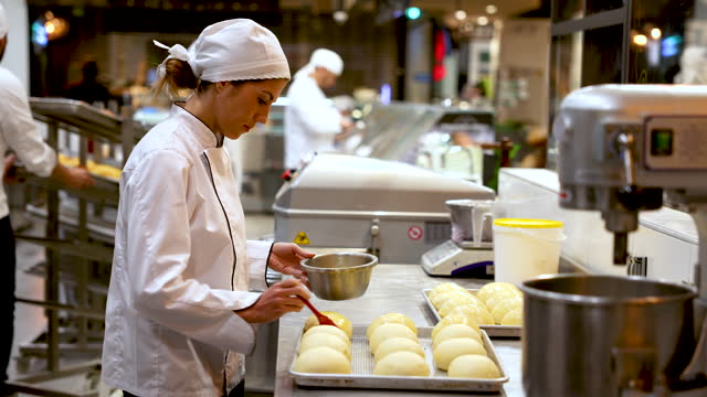 Young female baker spreading egg wash on raw bread before baking