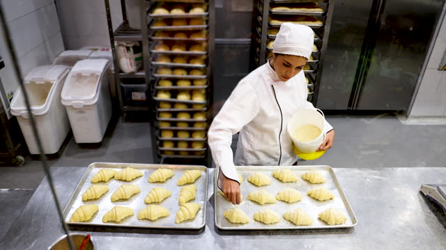 Happy Latin American female baker sprinkling coconut on croissants while working at a pastry shop
