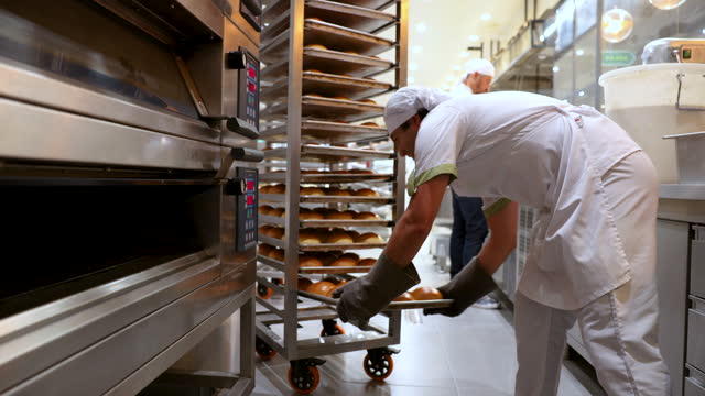 Cheerful baker taking out trays of fresh baked bread from the oven looking very happy