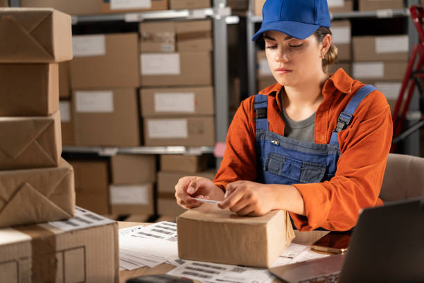 istock Online store owner sticking a barcode label on package box. Businesswoman preparing an order for shipping in a storehouse. Female entrepreneurs running an e-commerce small business 1638276581