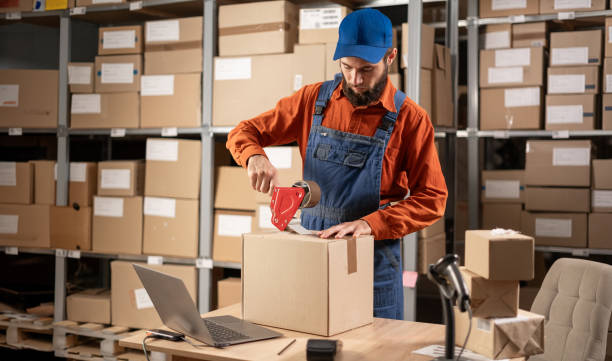 istock Warehouse male worker packing shipping ecommerce box checking website retail order preparing delivery parcel on table. 1638287407