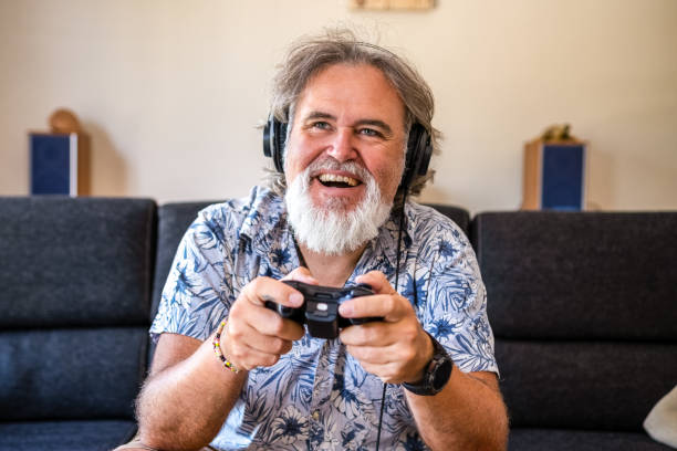 A 50 year old man looking like a happy badass enjoys playing video games in his living room stock photo