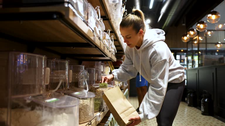 Sportswoman buying pumpkin seeds by bulk at an organic market adding them to a paper bag