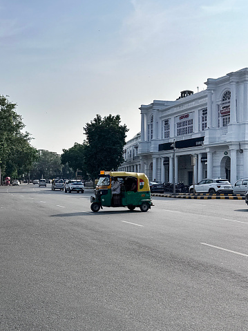Connaught Place, New Delhi, India - July 26, 2023: Stock photo showing auto rickshaw driving across road lanes and transporting passengers from Connaught Place, one of the largest business, commercial and financial centres in New Delhi, India.