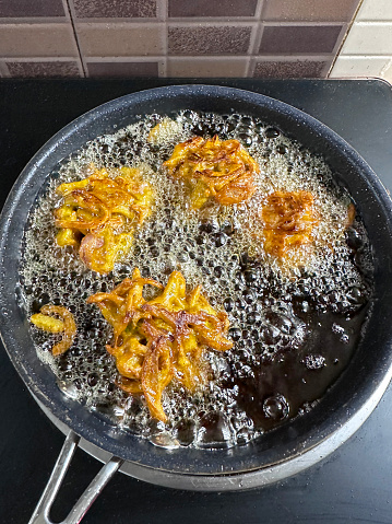 Stock photo showing elevated view of hot frying pan of bubbling cooking oil with frying homemade crispy onion bhaji pakoras recipe.