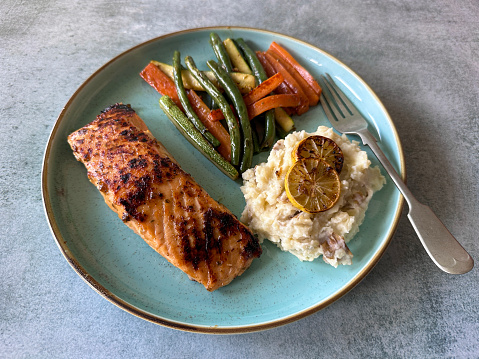 Stock photo showing close-up, elevated view of a healthy meal consisting of a dry fried salmon fillet served with mashed potatoes and roasted vegetables including courgette, carrot and green beans. This dish is part of a healthy eating, low calorie diet plan.