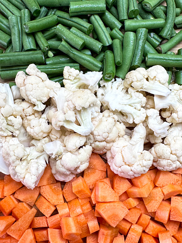 Stock photo showing a close-up, elevated view of rows of chopped vegetables displayed on a wooden chopping board. Green beans, white cauliflower florets and orange carrots for the stripes of the National flag of India (tricolour).