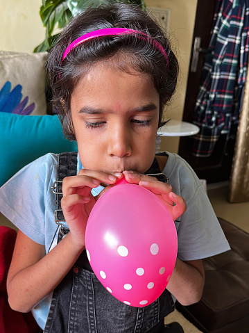 Stock photo showing close-up view of an Indian girl sitting on sofa whilst inflating a party balloon.
