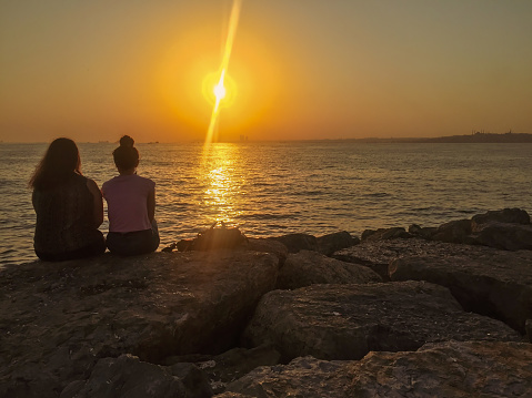 As the sun hovers on the verge of setting, two ladies find solace and tranquility as they sit serenely upon the rocks