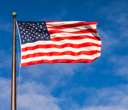 USA America flag waving in the wind over cloudy sky low angle view.