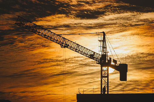 A worker guides the crane on a construction site at sunset