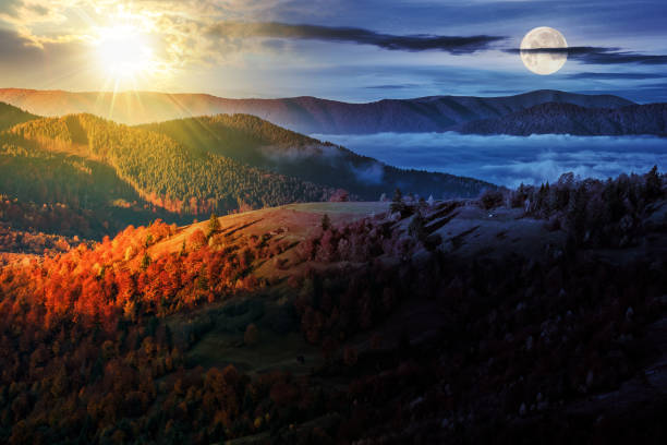 cold fog in the rural valley of Carpathian mountain range with sun and moon at twilight stock photo