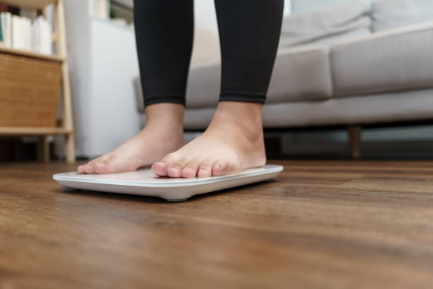 istock Fat diet and scale feet standing on electronic scales for weight control. Measurement instrument in kilogram for a diet control. 1638415908