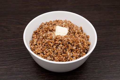 Buckwheat with butter in a white plate. Buckwheat porridge on a brown background. Vegetarian breakfast. dietary product