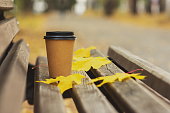 coffee cup and yellow leaves on a bench in an autumn park, autumn season concept