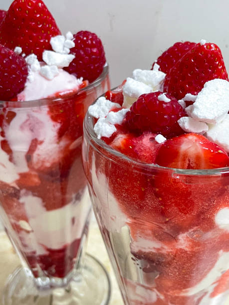 istock Image of two knickerbocker glasses filled with Eton mess dessert, mixed strawberries, whipped cream and broken meringue pieces, raspberry garnish, white background, focus on foreground 1638435881