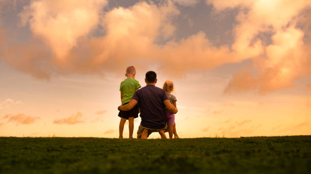 Father, son and daughter watching beautiful sunset.