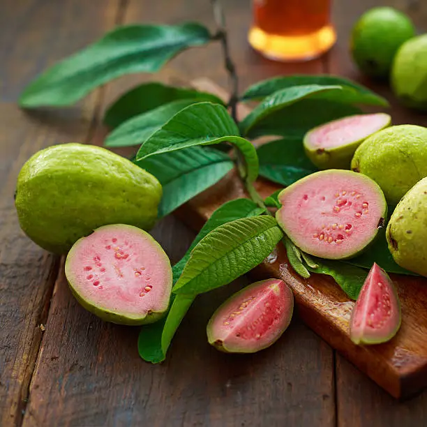 ripe guava fruits and real guava tree leaves over wooden background.