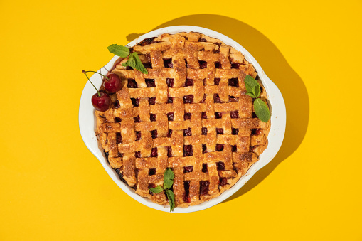 Piece of delicious homemade cherry pie with Flaky Crust sprinkled with sugar on the yellow bright background. American traditional cherry tart. Flat lay