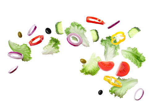 Lettuce leaves, olives, cut cucumber, onion, bell peppers and tomato falling on white background