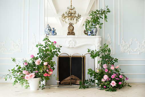 Bright luxury white and blue colored interior living room with flowers in vases. the walls are decorated with rococo. Vase with flowers on the background of a decorative fireplace in the living room.