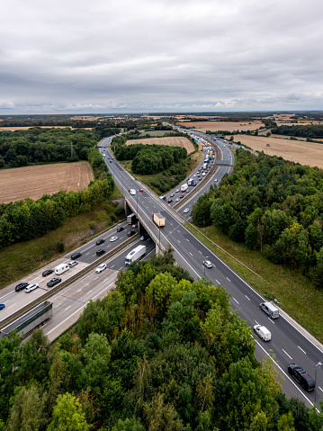 Aerial vertorama landscape of a busy stretch of the UK M1 motorway at a junction with traffic queuing and merging onto the main carriageway
