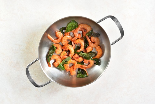 Garlic shrimps stir fry in pot over light background. Top view, flat lay