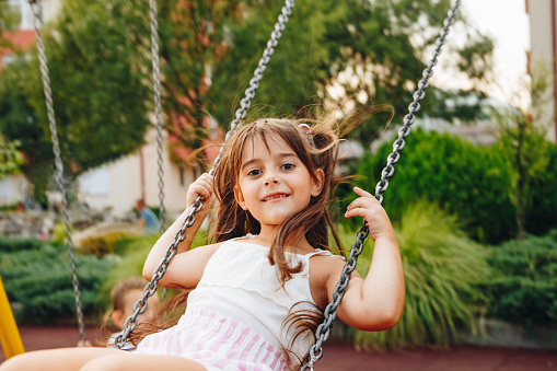 Father Pushing Children On Tire Swing In Garden