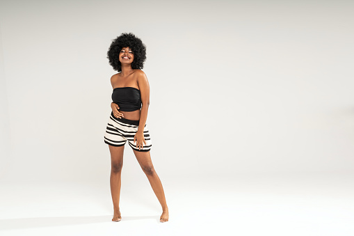 Fashionable happy woman with afro hairstyle wearing casual clothes, looking at the camera with big smile. Full length photo. Studio background. Copy space.