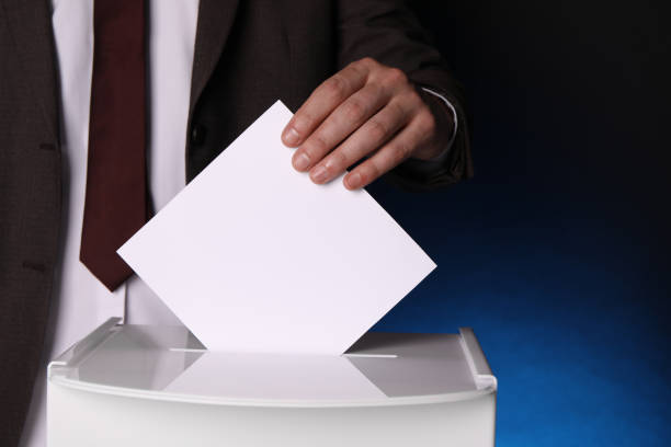 istock Man putting his vote into ballot box on dark blue background, closeup. Space for text 1638750423