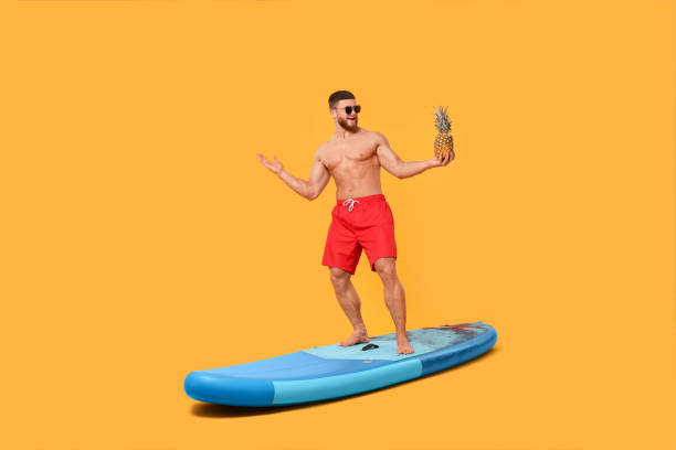 istock Happy man with pineapple posing on SUP board against orange background 1638750961