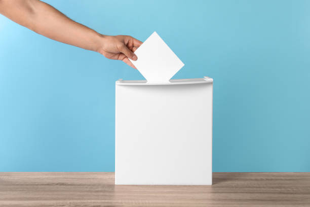 istock Man putting his vote into ballot box on light blue background, closeup 1638752057