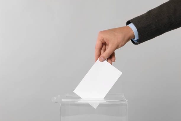istock Man putting his vote into ballot box on light grey background, closeup. Space for text 1638753092